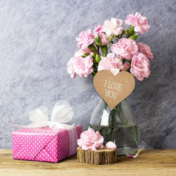 Vaasje met roze bloemen en een hartvormig label met de tekst 'I LOVE YOU', naast een cadeauverpakking