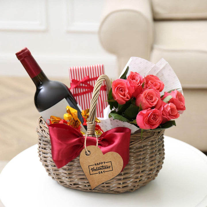 Rieten cadeaumand met fles wijn, bloemen, cadeautjes en een hartvormig cadeaulabel met tekst.
