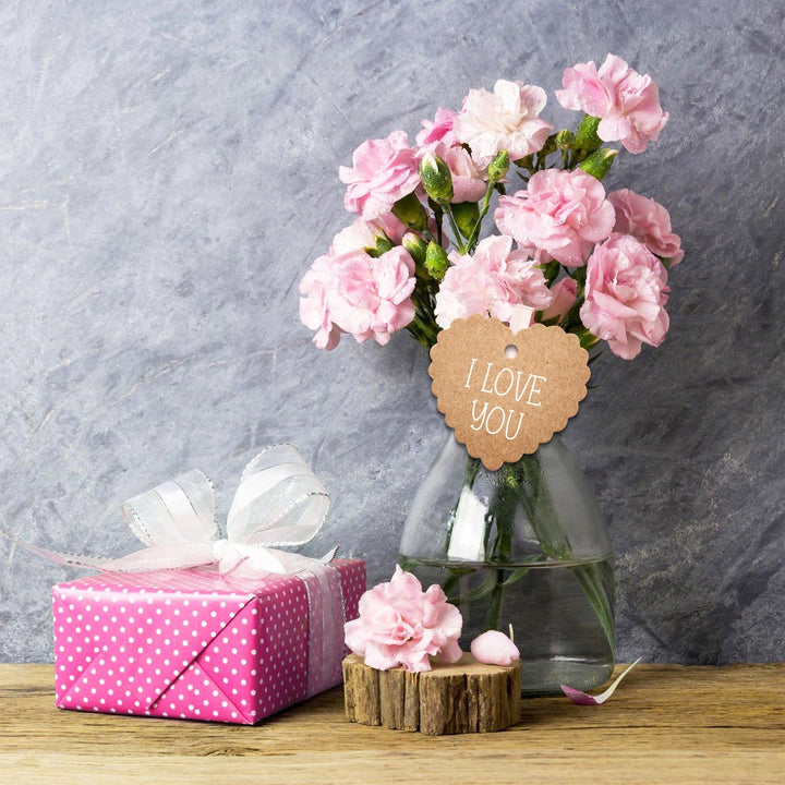Glazen vaas met roze bloemen en een gekarteld hartvormig label met tekst 'I LOVE YOU
